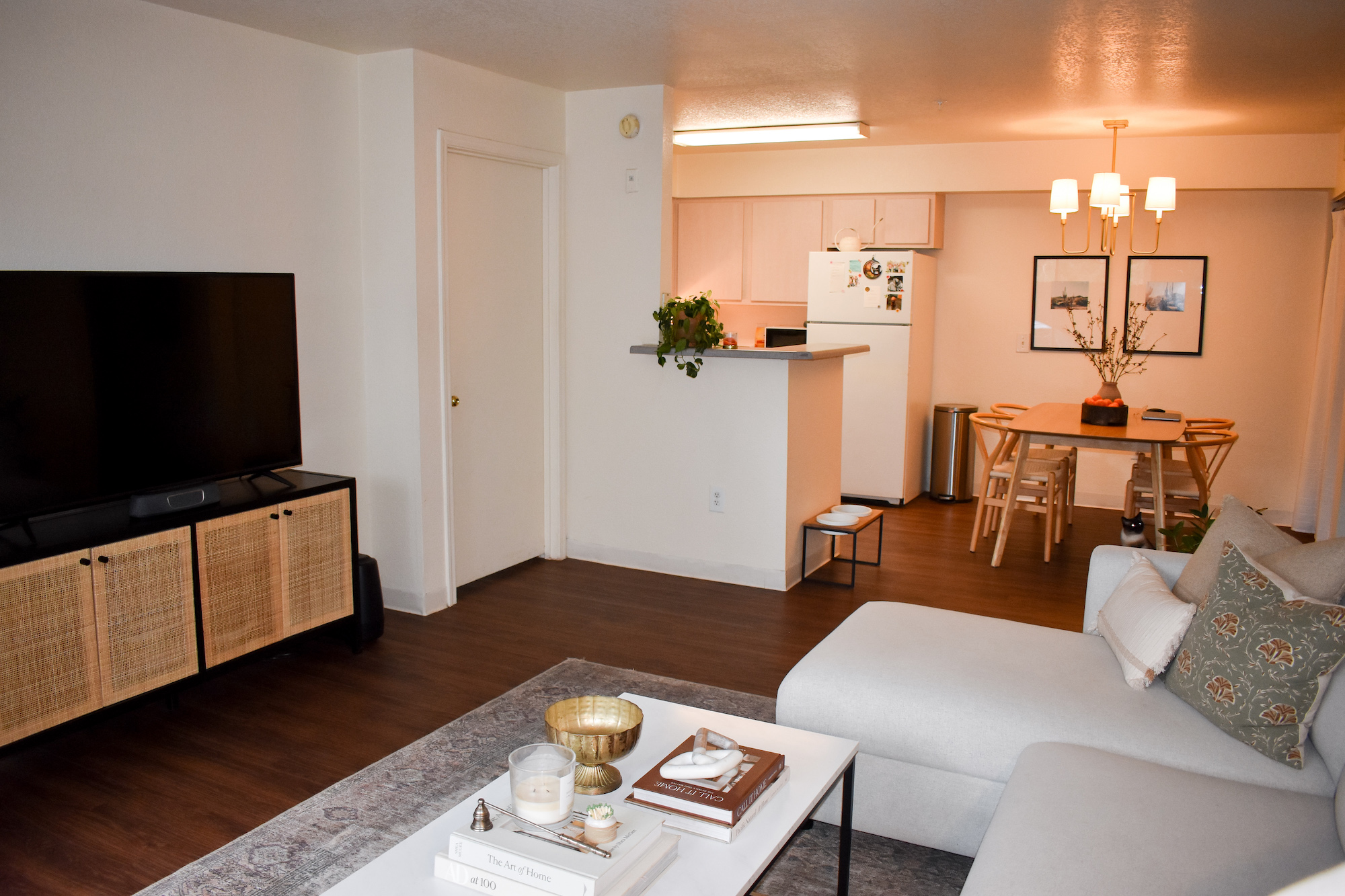 Living room setup with TV, couch, and dining room next to kitchen in background