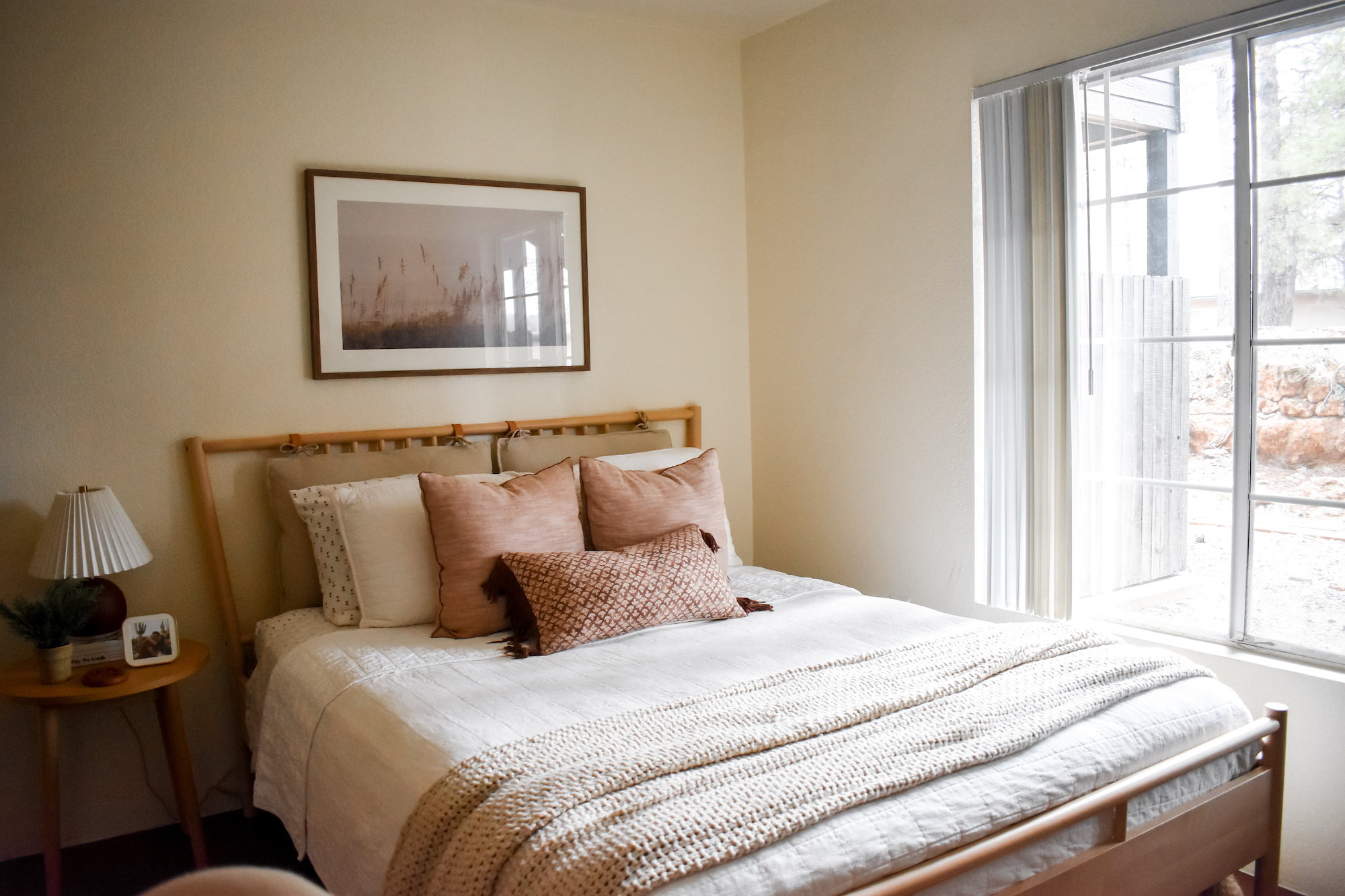 View of cozy bedroom with neutral bed setup and open window