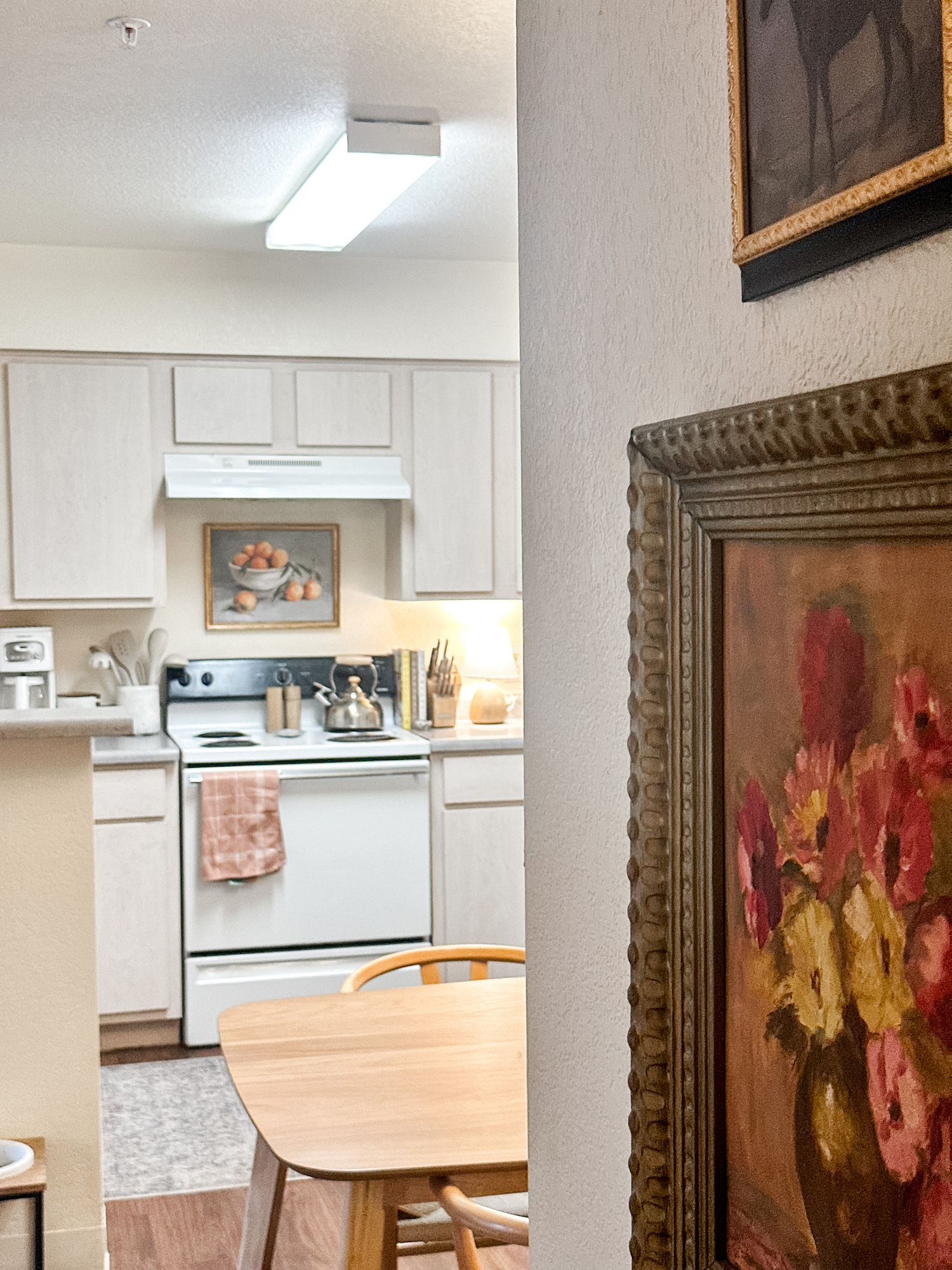 View of kitchen in distance from hallway with vintage inspired paintings hanging on wall